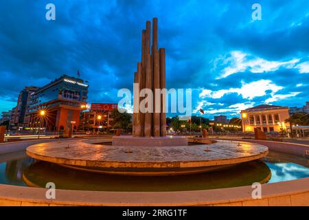 Shkoder, Albania - 1° maggio 2023: Nel cuore di Scutari, un vivace paesaggio urbano prende vita al calar della notte. Una fontana del centro offre una pittoresca Foto Stock