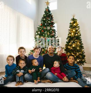 Famiglia diversificata insieme sotto gli alberi di natale nella loro casa Foto Stock