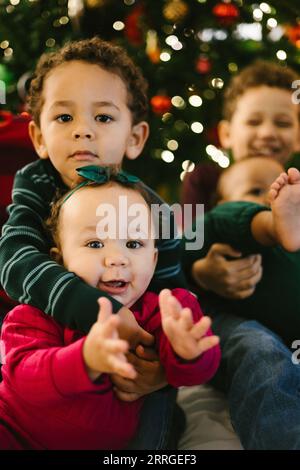 Il bambino tiene la sorellina mentre sorride con i fratelli a natale Foto Stock