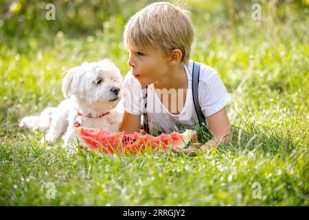 Fantastico bambino biondo, ragazzo con cane, anguria in giardino, estate Foto Stock