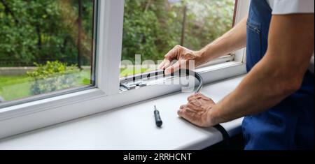lavoratore che installa nastro sigillante sul telaio della finestra in plastica. striscione con spazio per la copia Foto Stock