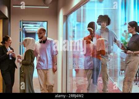 Tra le moderne pareti di vetro di un ufficio startup, un gruppo eterogeneo di colleghi, tra cui un uomo afroamericano, si impegnano in un caffè alimentato Foto Stock