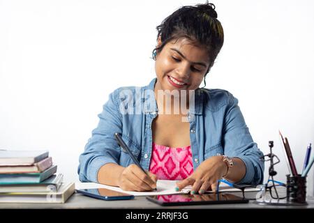 Un giovane studente indiano che studia e scrive su un tavolo da studio e su uno sfondo bianco Foto Stock