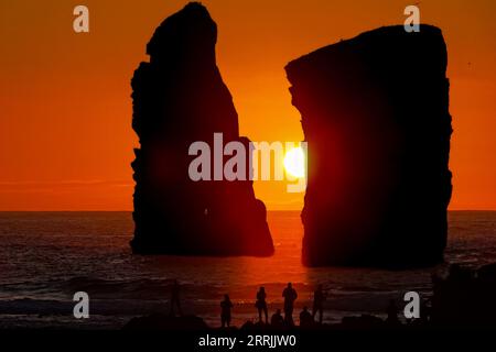 Le persone si riuniscono per osservare le enormi pile di mare che si stagliano davanti al tramonto su Ponta dos Mosteiros a Sao Miguel, Azzorre, Portogallo. Foto Stock