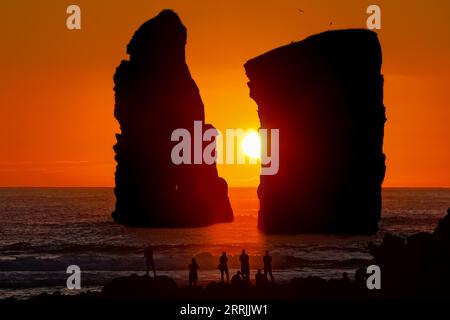 Le persone si riuniscono per osservare le enormi pile di mare che si stagliano davanti al tramonto su Ponta dos Mosteiros a Sao Miguel, Azzorre, Portogallo. Foto Stock