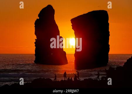 Le persone si riuniscono per osservare le enormi pile di mare che si stagliano davanti al tramonto su Ponta dos Mosteiros a Sao Miguel, Azzorre, Portogallo. Foto Stock