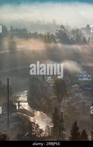 Città vecchia con la valle nebbiosa del fiume al mattino. Campagna dei Carpazi. Foto verticale Foto Stock