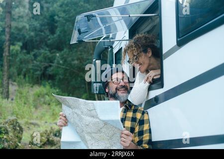 Felice coppia matura si diverte a viaggiare in camper vanlife, a parlare e a cercare insieme una guida per scegliere la prossima destinazione di vacanza. Uomo fuori e donna alla finestra. Camper Foto Stock