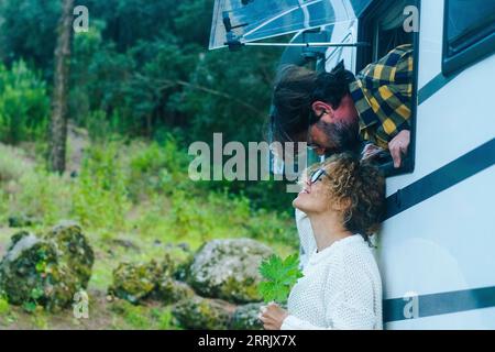 Coppia matura felice apprezza lo stile di vita dei camper vanlife in vacanza. Uomo fuori e donna alla finestra. Camper Foto Stock