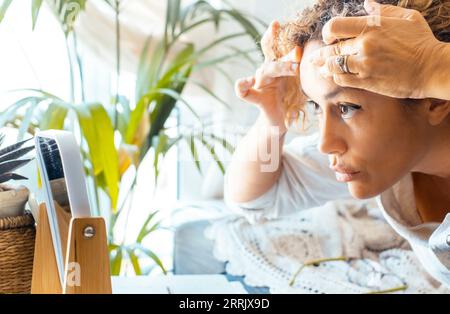 Primo piano di una donna adulta che controlla la faccia per verificare la presenza di rughe. Problema di invecchiamento. Una donna caucasica di mezza età che guarda se stessa su uno specchio a casa. Stile di vita quotidiano per la cura della pelle. Donna preoccupata che guarda Foto Stock