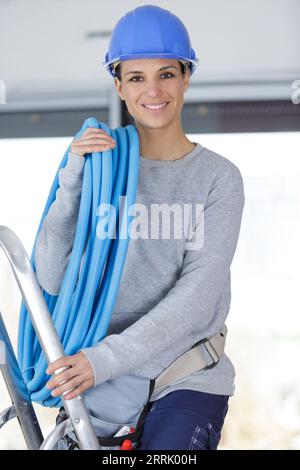 idraulico femmina su scala che trasporta il tubo blu Foto Stock