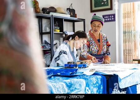 220822 -- GUIYANG, 22 agosto 2022 -- la madre di Zhang Juanjuan le ordina di fare un dipinto batik in uno studio batik ad Anshun, nella provincia di Guizhou nella Cina sud-occidentale, 18 agosto 2022. Zhang Juanjuan, una ragazza del gruppo etnico Miao, ha deciso di tornare a casa per rilevare i suoi affari dei genitori relativi alla produzione di prodotti batik dopo la laurea. Il batik è un patrimonio culturale intangibile nella sua città natale. Ha registrato il laboratorio batik dei suoi genitori come una società d'arte batik e ha fondato il suo studio batik fai da te. Per espandere la propria attività, Zhang Juanjuan e i suoi colleghi hanno progettato un modello pratico e rispettoso dell'ambiente Foto Stock