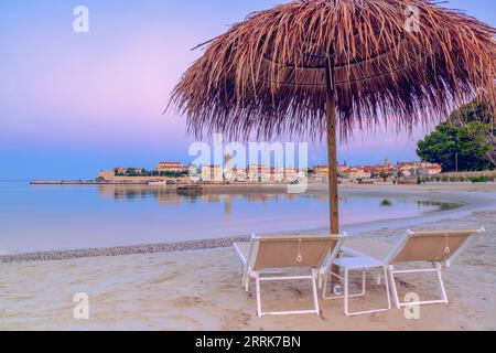 Europa, Croazia, Primorje-Gorski Kotar County, isola di Rab, sdraio e ombrelloni sulla spiaggia sabbiosa che si affaccia sul centro storico di rab sullo sfondo Foto Stock