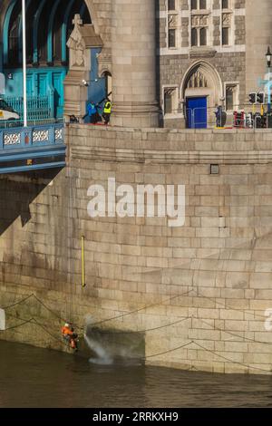 Inghilterra, Londra, Tower Bridge, addetti alla manutenzione che utilizzano il tubo dell'acqua ad alta pressione per pulire la base del ponte a bassa marea Foto Stock