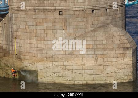 Inghilterra, Londra, Tower Bridge, addetti alla manutenzione che utilizzano il tubo dell'acqua ad alta pressione per pulire la base del ponte a bassa marea Foto Stock