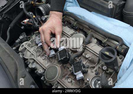Vista, CA USA - 3 settembre 2023: Il meccanico stringe manualmente il dado sulla bobina di accensione appena installata su un motore Volvo Foto Stock