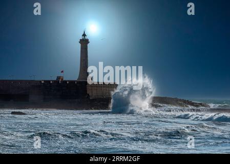 La luna splende su un pittoresco faro di notte, le onde si infrangono sulla costa Foto Stock