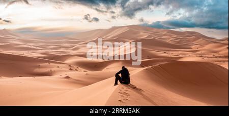 Una persona seduta nel deserto di Erg Chebbi nel Sahara africano, in Marocco Foto Stock