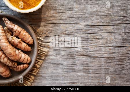 Radice di curcuma fresca e polvere di curcuma essiccata su uno sfondo rustico in legno con spazio per la copia, vista dall'alto Foto Stock