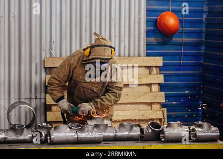 Lavoratore maschio che rettifica parti di tubi a T in fabbrica. Foto Stock