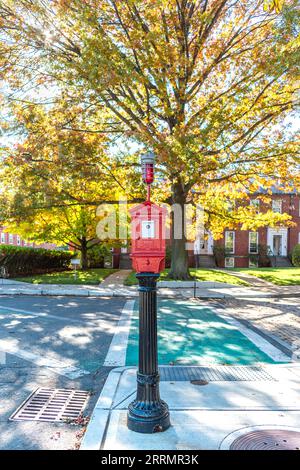 Scatola tradizionale per la stazione di allarme antincendio di Boston - prodotta da Game Well - su un piedistallo di fronte a splendidi alberi d'autunno in una soleggiata giornata autunnale Foto Stock