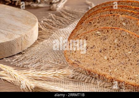 Fette di pane di segale fresco con i grani giacciono su un tovagliolo da burlap, in stile rustico ravvicinato. Foto Stock