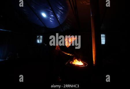 230113 -- GENHE, 13 gennaio 2023 -- Juele fa bollire il tè al latte in una tenda prima dell'alba in una stazione temporanea di allevamento nella catena forestale di Jinhe vicino a Genhe City, regione autonoma della Mongolia interna della Cina settentrionale, 12 gennaio 2023. Ogni due o tre giorni, Juele Bulituotian si dirigerà verso la catena forestale di Jinhe a circa 80 chilometri da Genhe City. E' qui che il 39enne allevatore Aoluguya Ewenki, che indossa un tradizionale cappotto di pelliccia, troverà le sue renne da foraggiatore. Invece di tenere le renne in un fienile, i pastori Ewenki lasciano che gli animali vivano nella foresta e li controllano ogni due giorni. Juele possiede oltre 60 rei Foto Stock