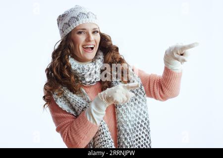 Ciao inverno. donna moderna sorridente con maglione, guanti, cappello e sciarpa che puntano allo spazio per la copia su sfondo bianco. Foto Stock