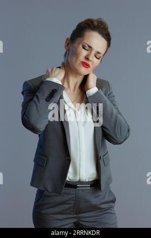 lavoratrice donna moderna stanca in costume grigio con dolore al collo isolato su sfondo grigio. Foto Stock