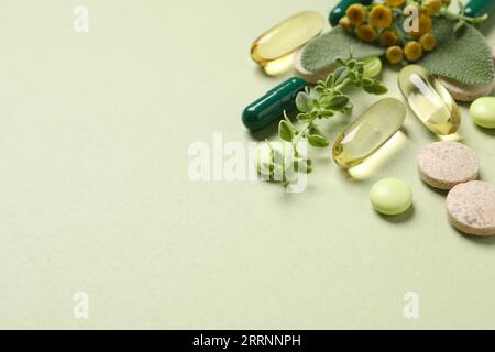 Pillole ed erbe diverse su sfondo verde chiaro, spazio per il testo. Integratori alimentari Foto Stock