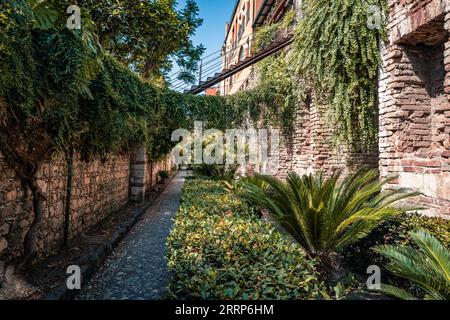 pareti in pietra e mattoni lungo marciapiede pavimentato con alberi in una soleggiata giornata estiva Foto Stock