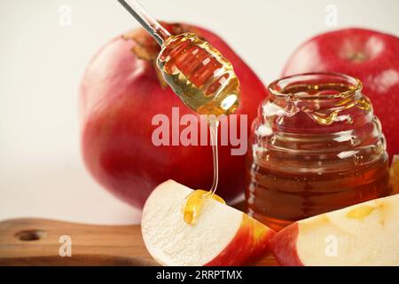 Festa ebraica Rosh Hashana. Melograno, mele e miele prodotti tradizionali per la vacanza. Versare il miele sulla mela e sul melograno Foto Stock