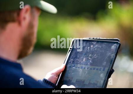 scienziato agronomo agricoltore che guarda campioni di terreno e erba in un campo in primavera. guardando la crescita delle piante e la salute del suolo, utilizzando un telefono e tec Foto Stock