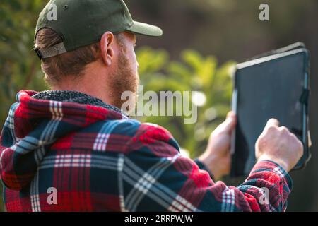 scienziato agronomo agricoltore che guarda campioni di terreno e erba in un campo in primavera. guardando la crescita delle piante e la salute del suolo, utilizzando un telefono e tec Foto Stock