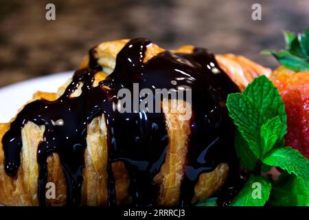 un sacco di condimento di cioccolato fondente versato su croissant fresco con menta e fragole su un piatto bianco cuocere a casa a chi piace troppo cioccolato al cioccolato non è mai troppo dolce Foto Stock