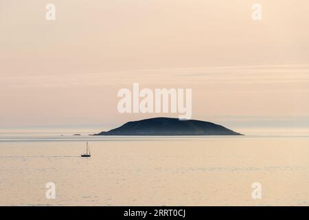 Una barca solitaria naviga sull'isola di Onza nella Ria de Pontevedra in Galizia durante il tramonto. Foto Stock