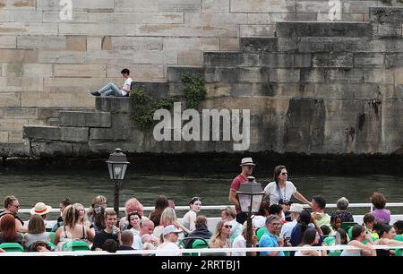 230713 -- PARIGI, 13 luglio 2023 -- Un uomo si riposa sulla Senna mentre una barca turistica passa accanto a lui a Parigi, in Francia, 28 giugno 2023. La Senna, il secondo fiume più grande della Francia, si snoda attraverso il cuore di Parigi. Scorrendo da ovest a est, divide la città nelle iconiche sponde sinistra e destra . La riva sinistra è caratterizzata da un'atmosfera artistica, adornata da caffè, teatri e librerie, che creano un paradiso per il circolo letterario e un paradiso culturale. D'altra parte, la riva destra ospita prestigiosi monumenti storici come il Louvre, l'ex palazzo reale e l'Elyse Foto Stock