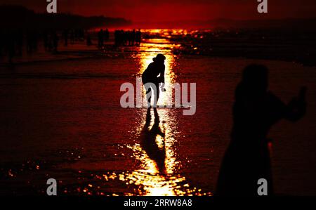 230814 -- DONGXING, 14 agosto 2023 -- Un turista si diverte all'alba sulla spiaggia di Jintan a Dongxing, nella regione autonoma del Guangxi Zhuang nel sud della Cina, 14 agosto 2023. La spiaggia di Jintan, situata nella parte meridionale dell'isola di Wanwei, ha una costa di 15 chilometri e prende il nome dal suo colore di sabbia dorata. CHINA-GUANGXI-DONGXING-JINTAN BEACH CN FEIXMAOHUA PUBLICATIONXNOTXINXCHN Foto Stock