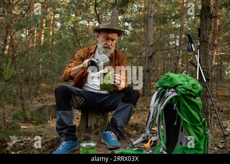 Viaggiatore anziano che usa un bruciatore a gas portatile per cucinare la cena Foto Stock