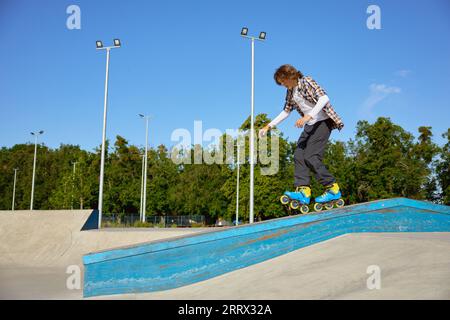 Un giovane ragazzo che indossa pattini in linea che fa acrobazie di equilibrio al parco skateboard Foto Stock