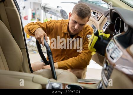 Uomo che aspira il sedile del conducente in auto utilizzando una soffiante portatile Foto Stock