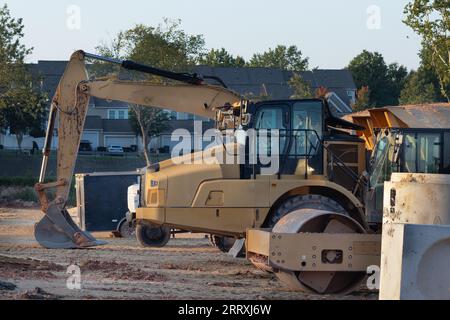 Camion e attrezzature per impieghi pesanti in un cantiere vicino a un quartiere residenziale. Foto Stock