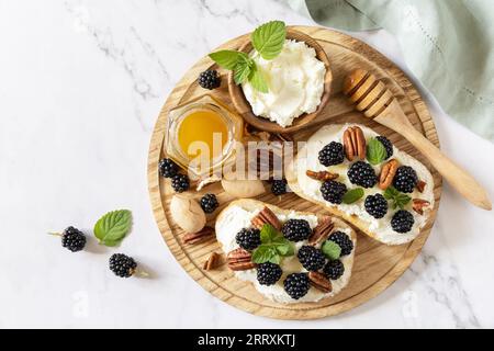 Brindisi salutari per la colazione. Panini con dieta Keto. Spuntino Keto. Bruschetta dolce con formaggio e frutti di bosco ricotta di mora e miele su tavola di marmo. Vie Foto Stock