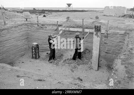Zwei Baurbeiter schaufeln Sand aus einer Grube auf der Baustelle von Lelystadhaven, 1955. Due operai edili lanciano la sabbia da una fossa nel cantiere di Lelystadhaven, 1955. Foto Stock