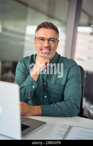 Uomo d'affari sorridente seduto al lavoro in ufficio, ritratto verticale. Foto Stock