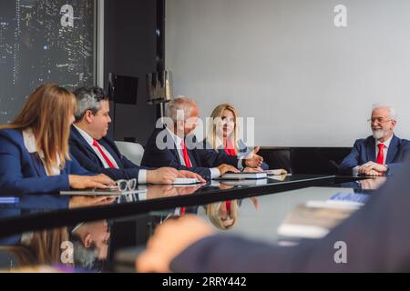 Il leader dell'azienda anziana è orgoglioso di ascoltare il suo dipendente maschio maturo che spiega i nuovi dettagli del progetto e i profitti durante la riunione al tavolo del Consiglio di amministrazione in mo Foto Stock