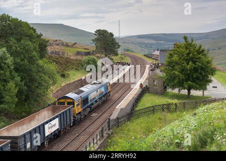 GB Railfreight classe 66 locomotiva diesel che trasporta un treno merci attraverso la stazione ferroviaria di Dent, Cumbria, Regno Unito sulla linea ferroviaria Settle to Carlisle Foto Stock