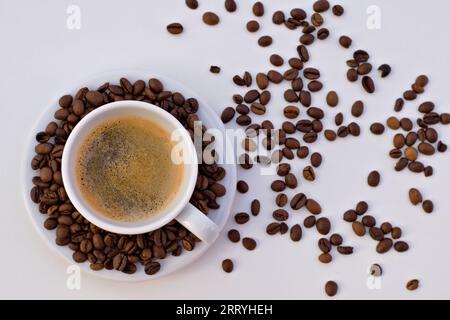 Tazza di caffè nero e piattino con chicchi di caffè su sfondo bianco. Foto Stock