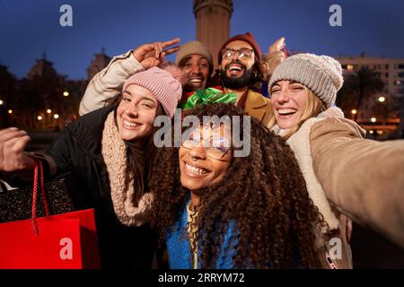 Selfie allegri e giovani gruppi multietnici che tengono in mano le borse della spesa regali di Natale. Felici amici inverno Foto Stock