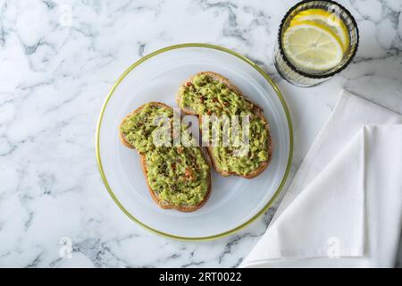 Deliziosi panini con guacamole e fette di limone in vetro su un tavolo in marmo bianco, piatti Foto Stock